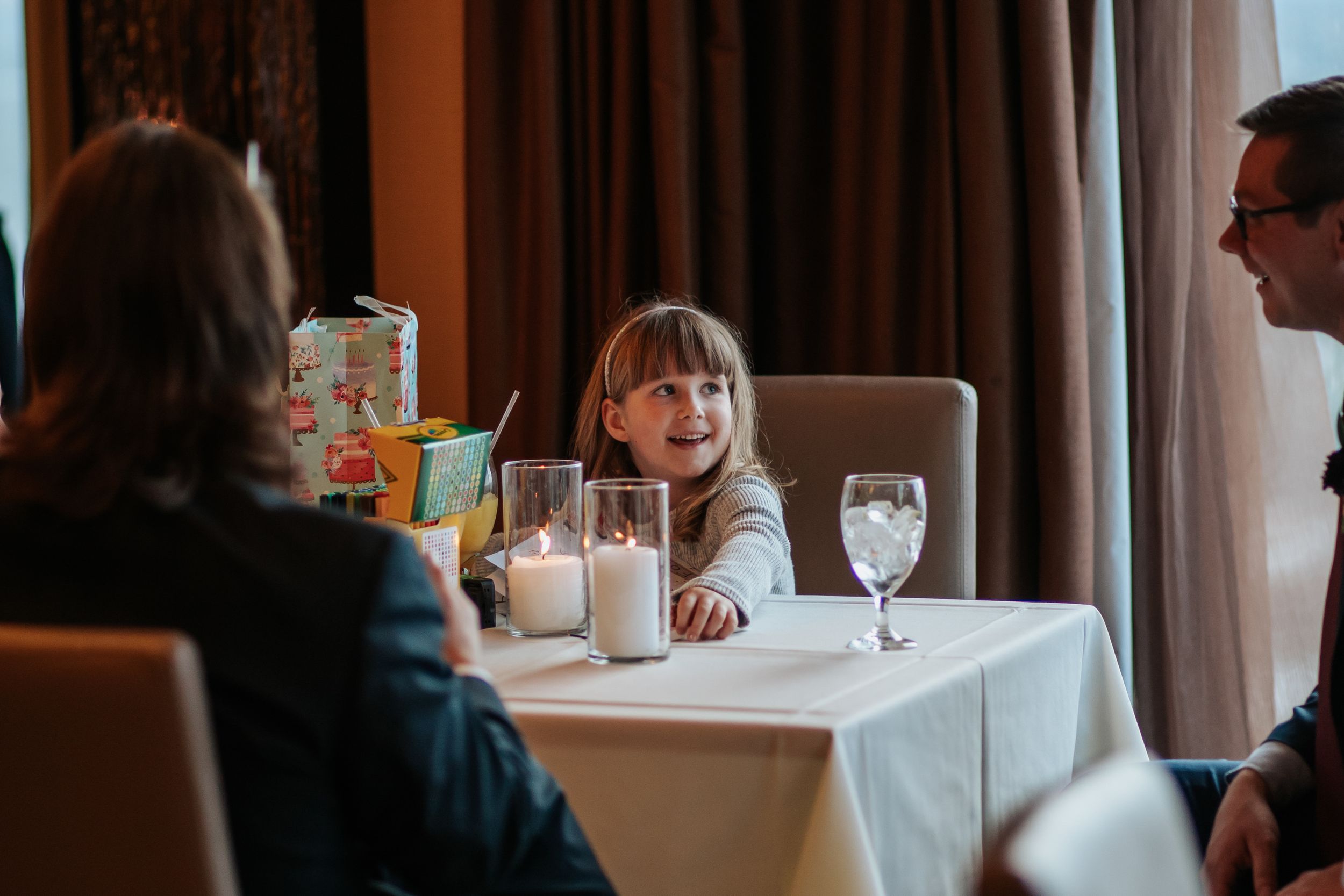 A group of people dine together at an elegant restaurant with white tablecloths and ambient lighting.