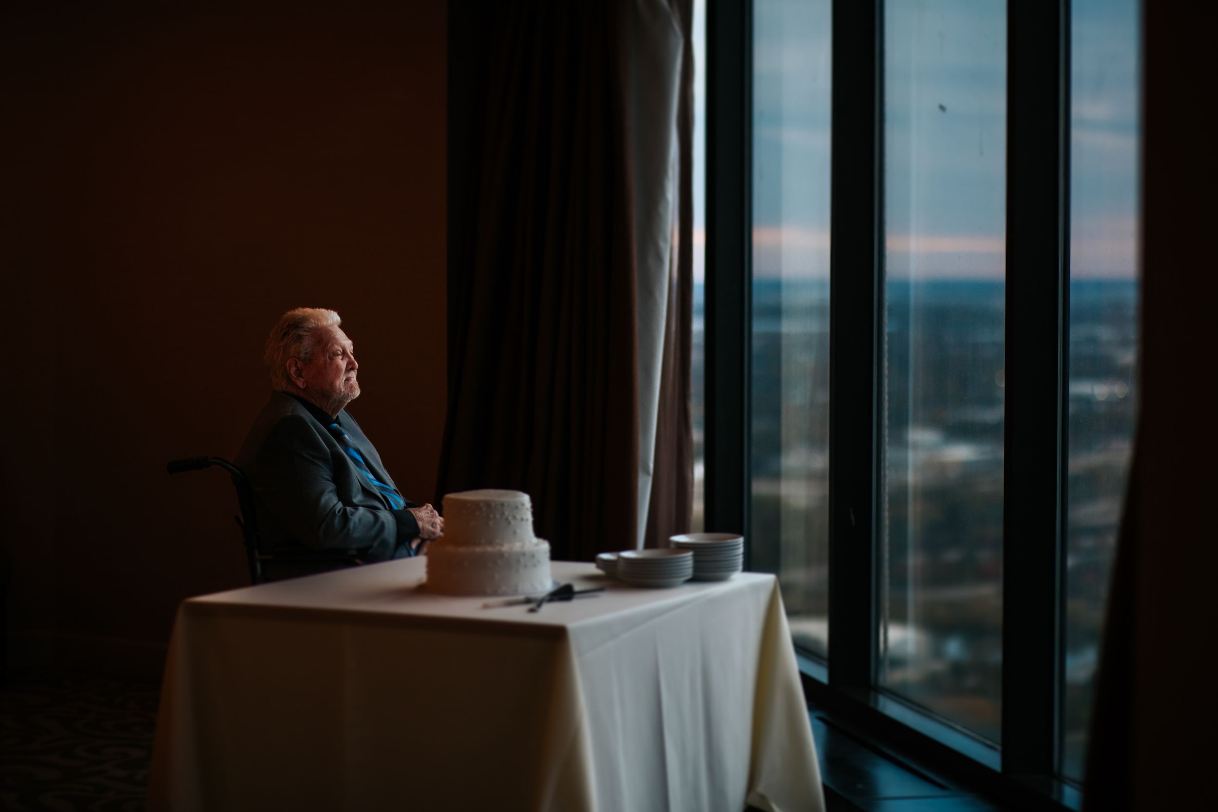 Person gazing out large windows of a modern high-rise building with city skyline views at sunset.