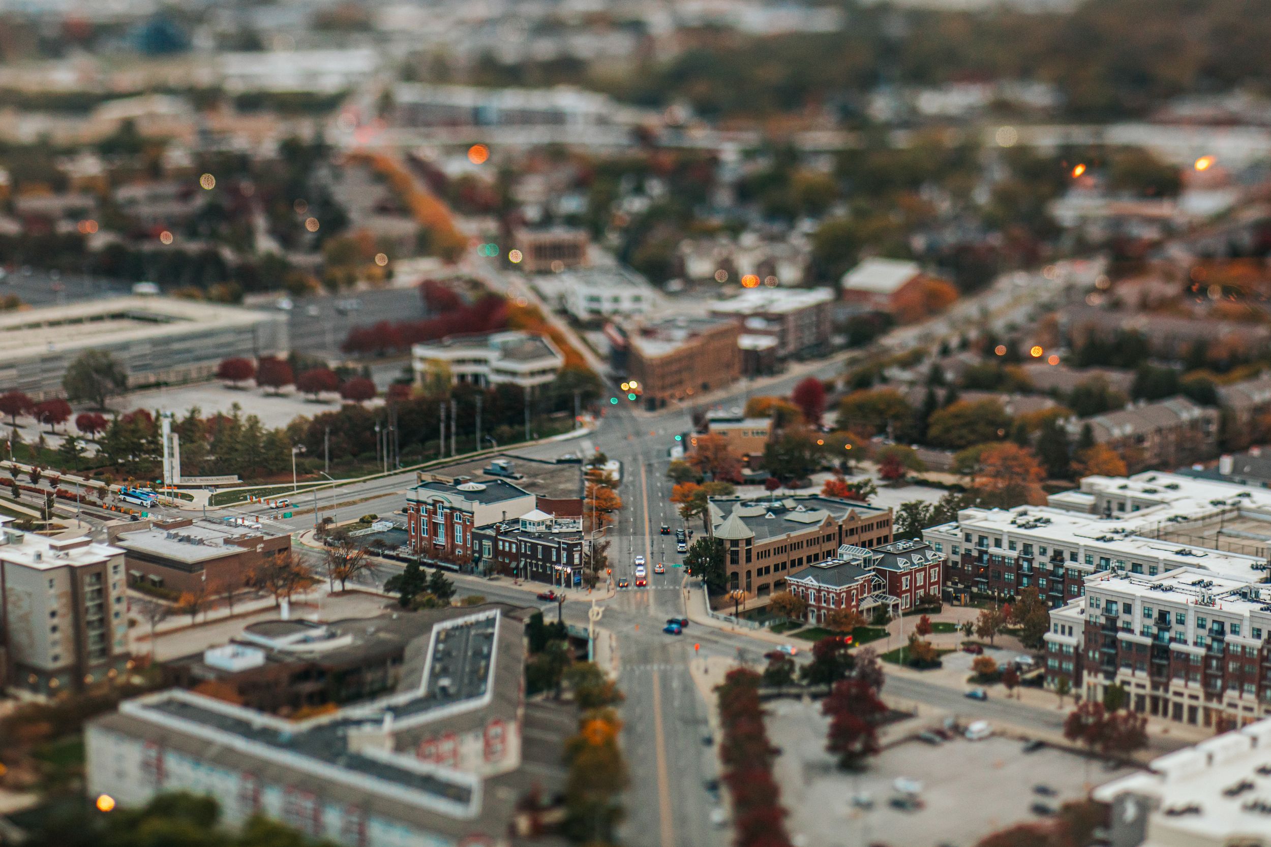 Aerial tilt-shift cityscape view showing urban buildings and streets with a miniature effect.