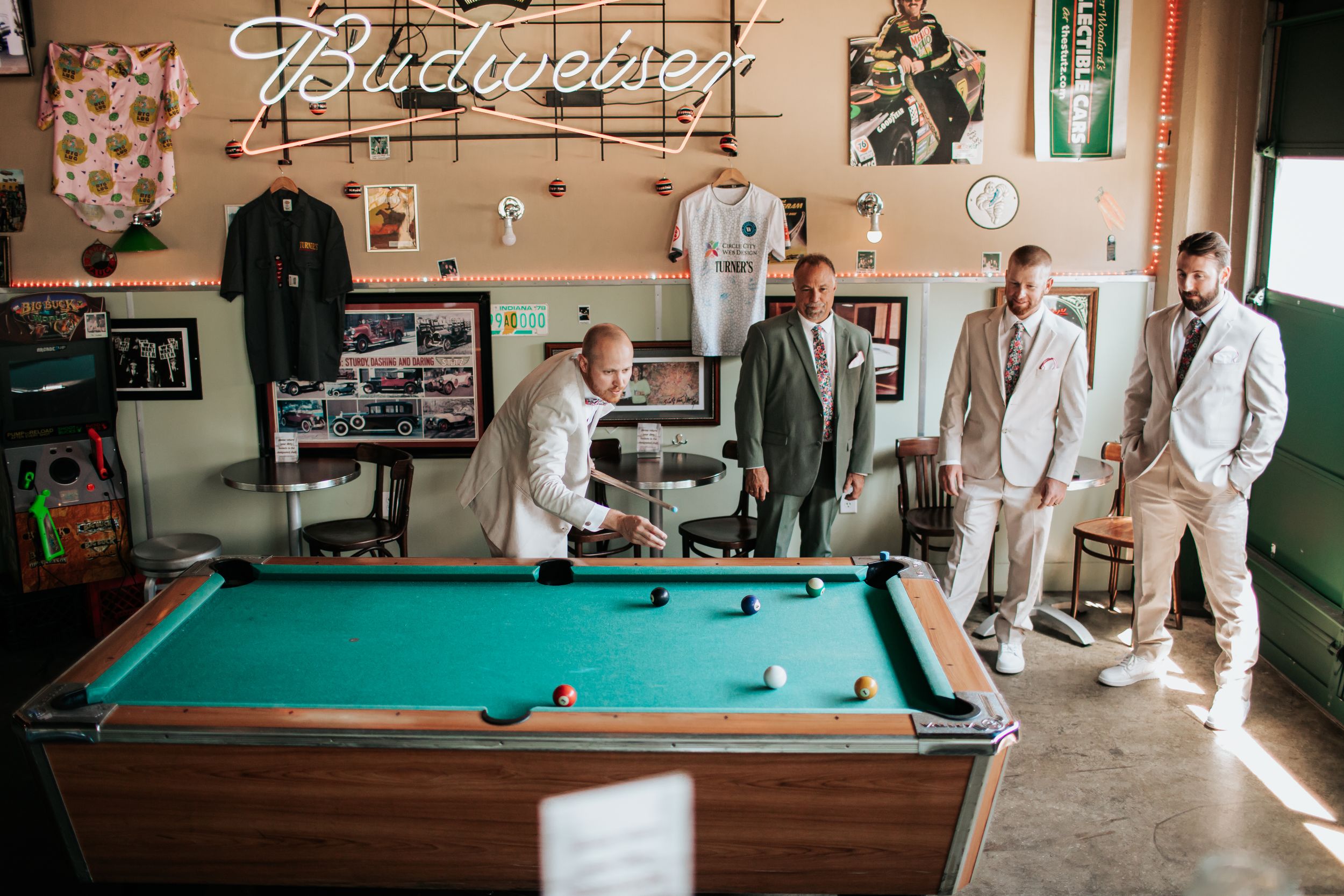 People playing pool in a rustic billiards room with vintage decor and natural lighting.