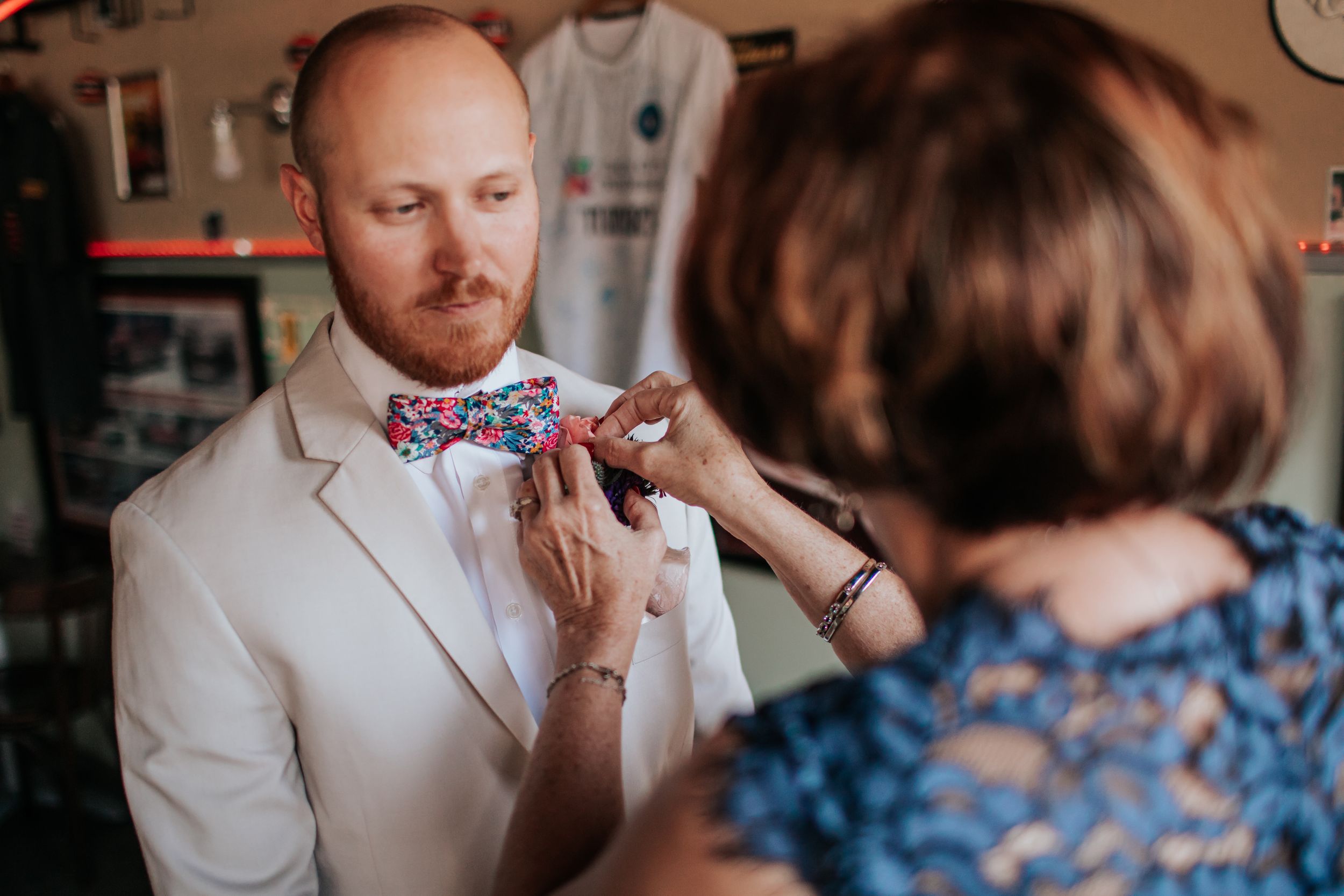 A sequence of images showing someone in a white suit adjusting a bowtie with help from another person.