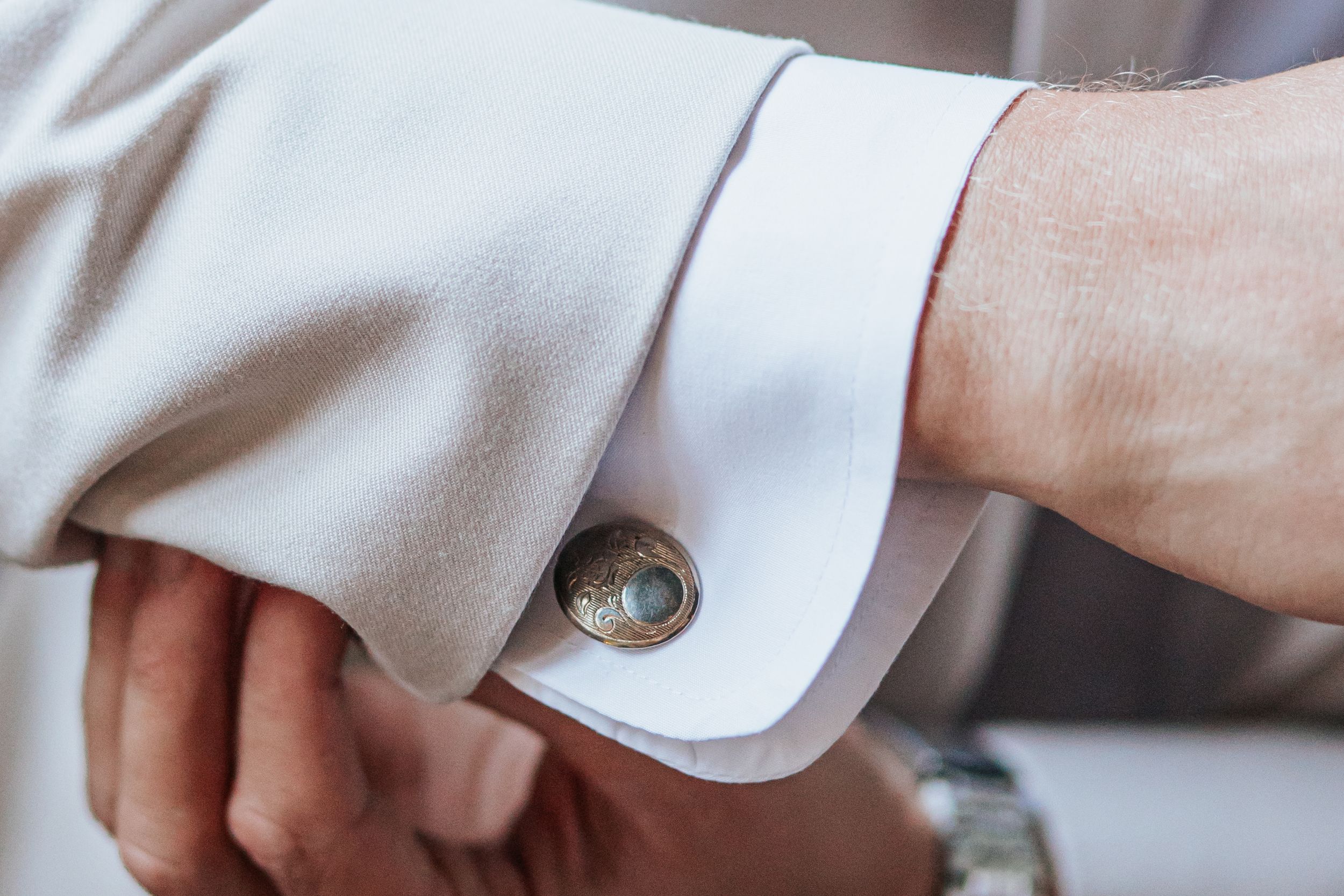 Close-up of hands adjusting white dress shirt cuffs with elegant cufflinks.