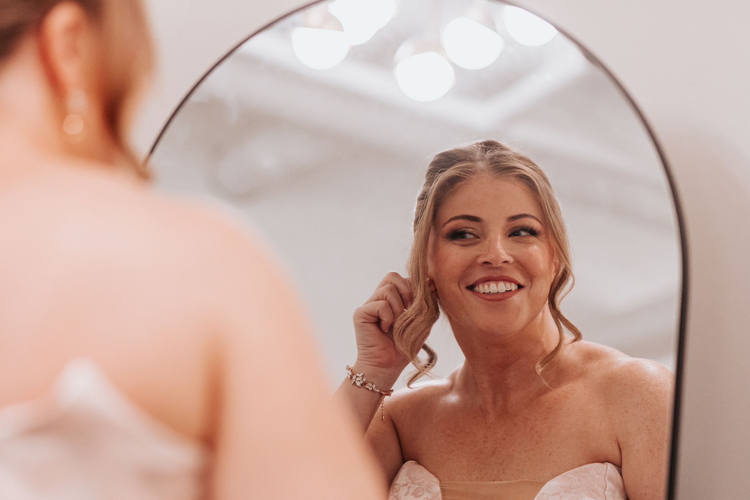 Reflection in mirror shows someone wearing a white dress and smiling while getting ready.