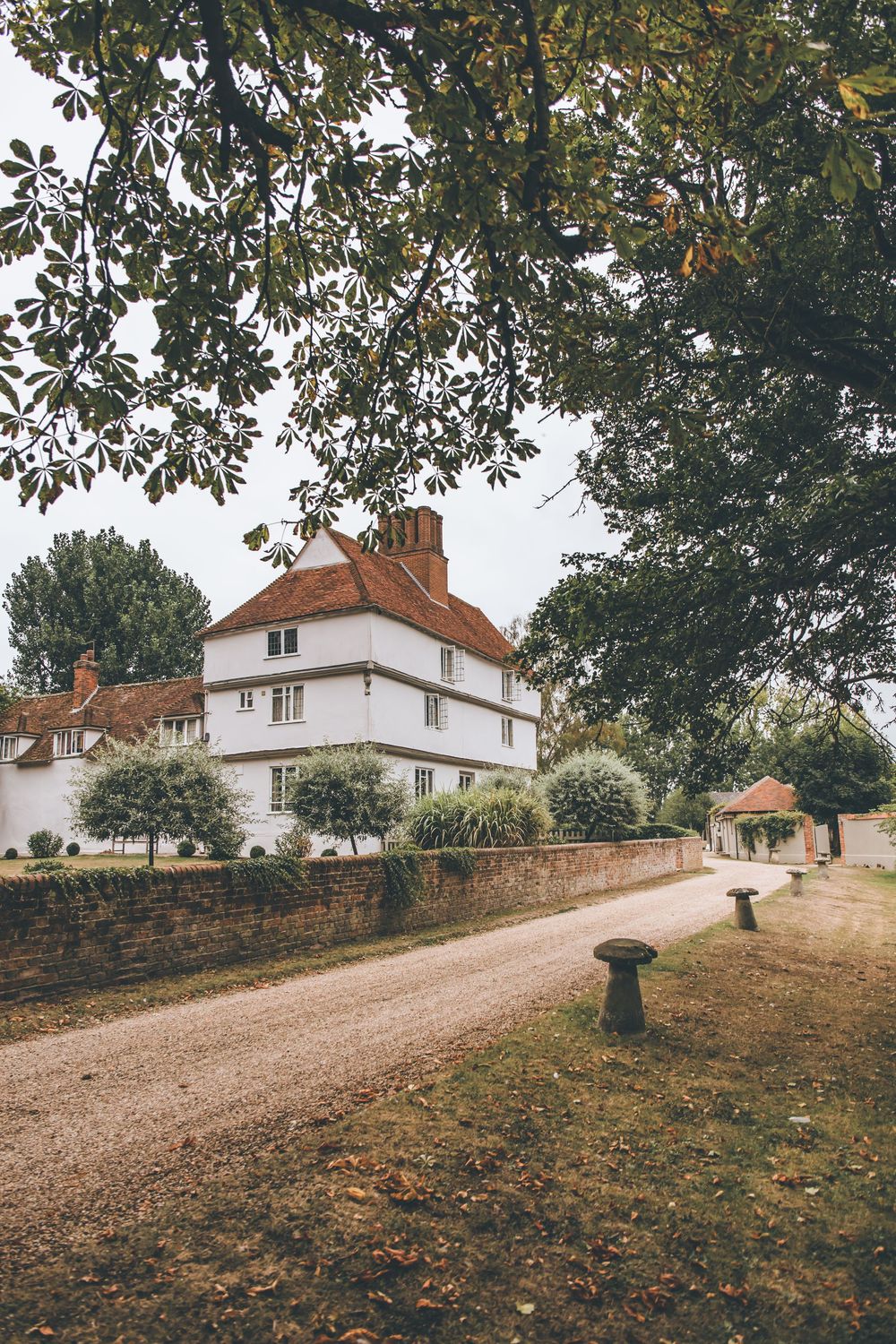 Panoramic view of a white country house with brick walls and gravel driveway.