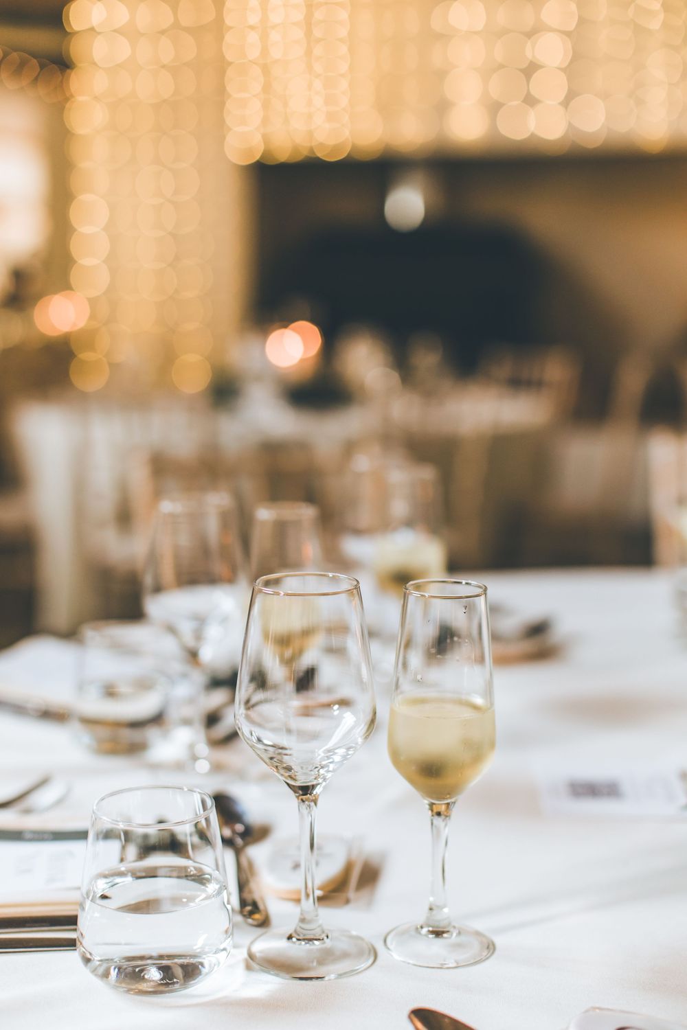 Elegant table setting with wine glasses and soft bokeh lighting creates a romantic wedding reception atmosphere.