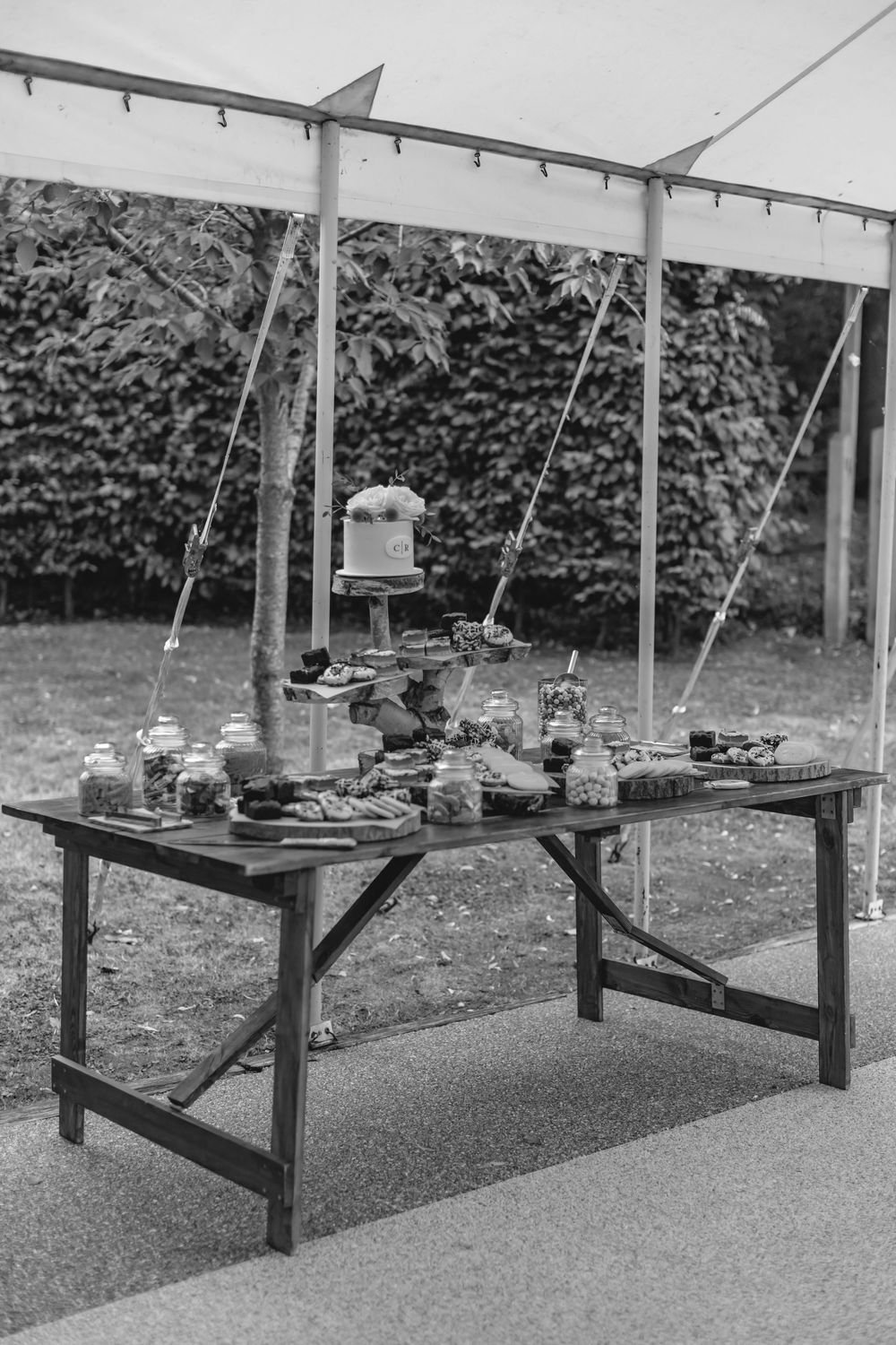 A rustic dessert table setup with cake stands and treats under an outdoor tent.