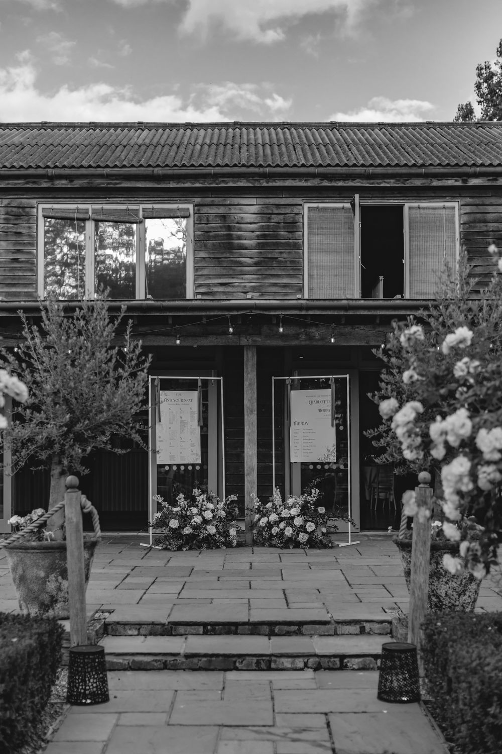 Black and white photo of a rustic wooden building with floral arrangements decorating the entrance.