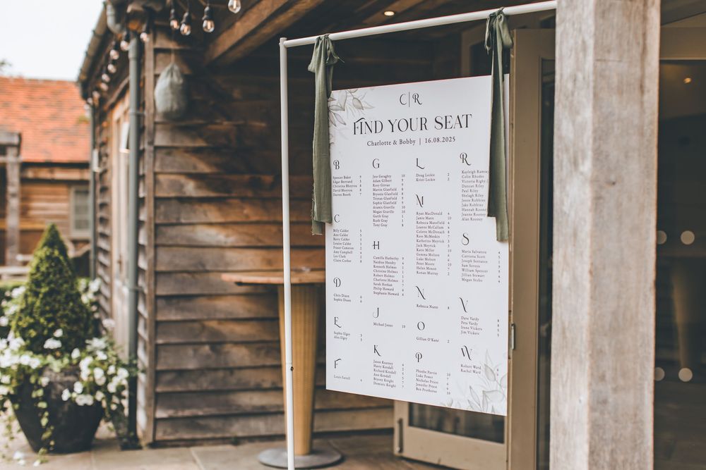 Wedding seating chart displayed on stand outside rustic wooden venue.