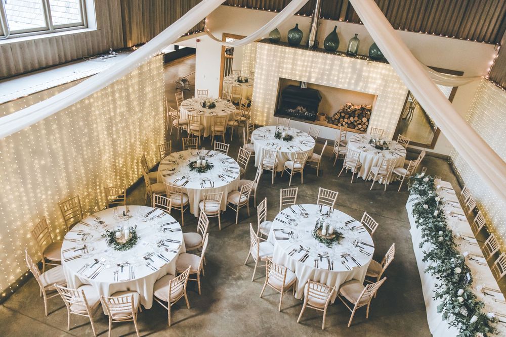 Rustic barn wedding venue with white tables and greenery decorations.