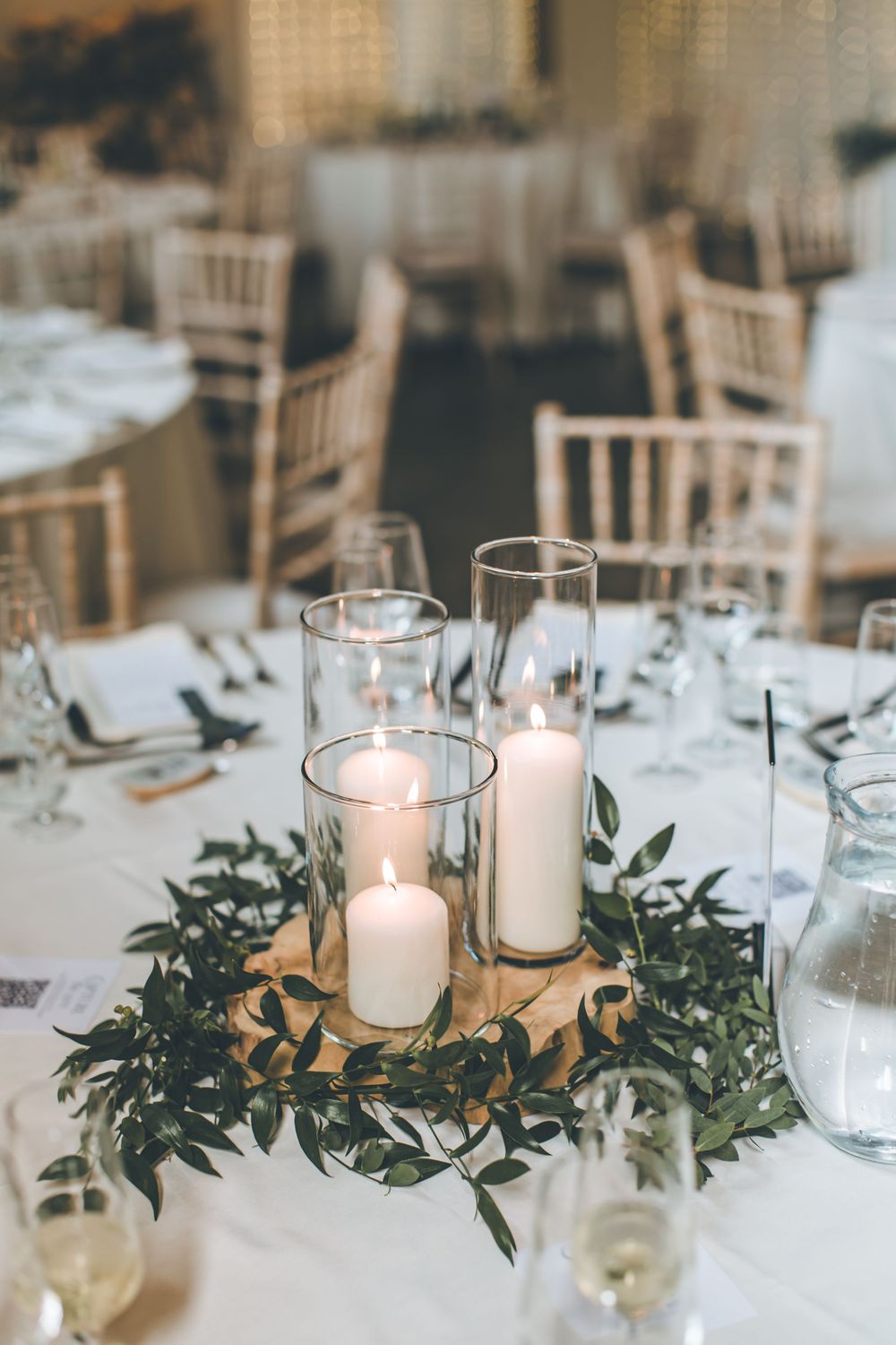 Elegant table settings with white candles and fresh greenery centerpieces.