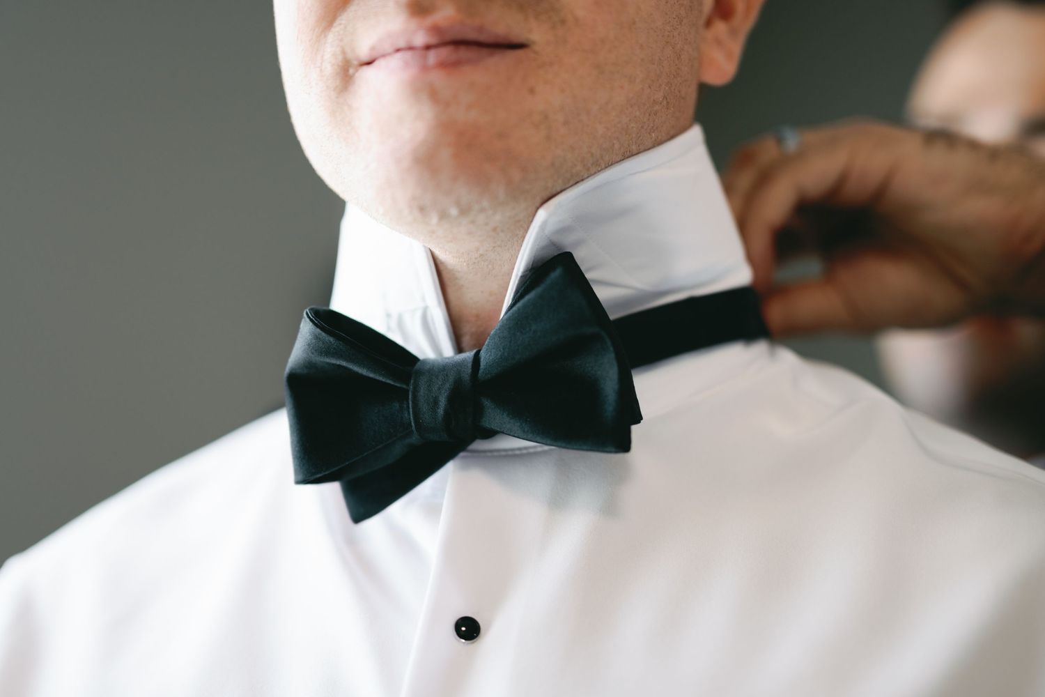 Close-up view of a black bowtie being adjusted on a formal white dress shirt.