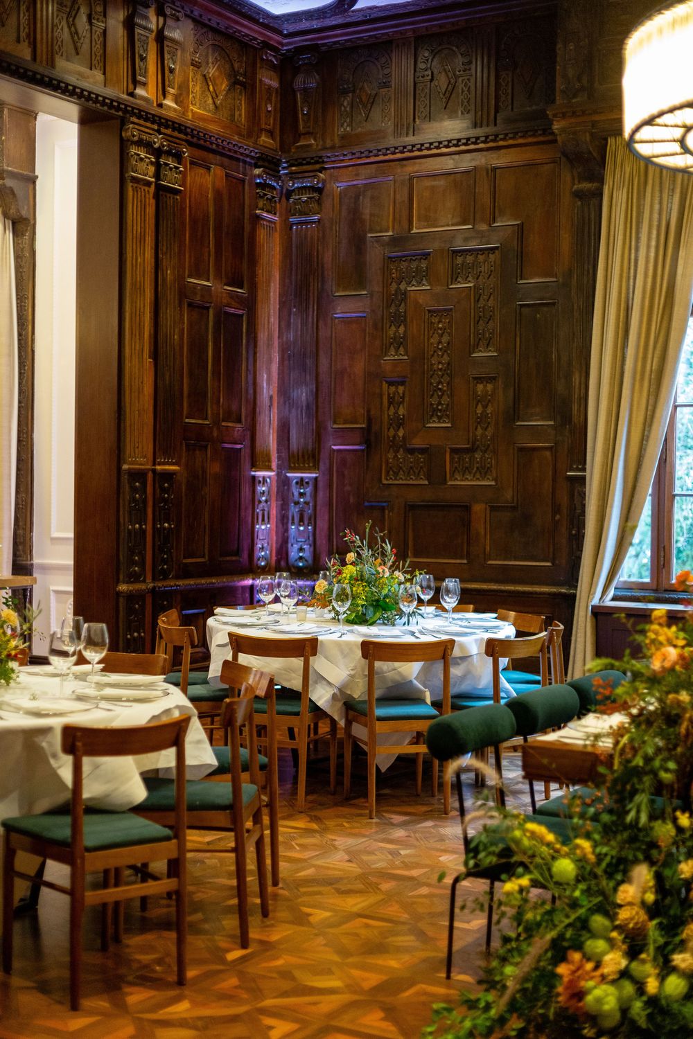Luxurious wood-paneled dining room with classic decor featuring elegant table settings and green upholstered chairs.