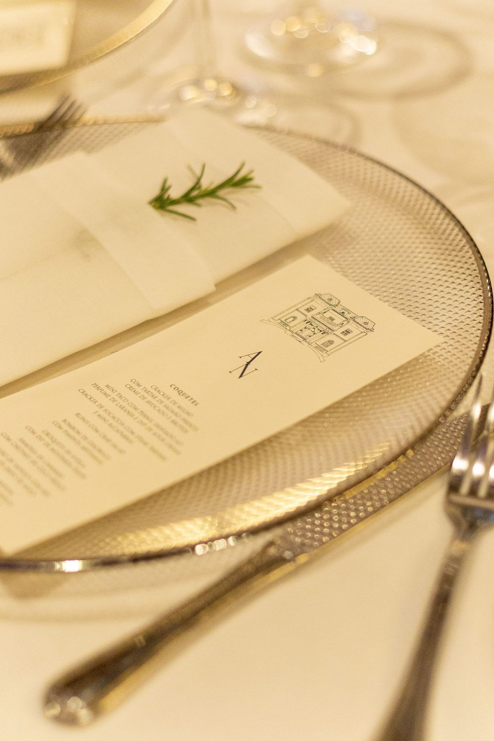 Elegant place setting at upscale restaurant with silver cutlery and white plates arranged on cream tablecloth.