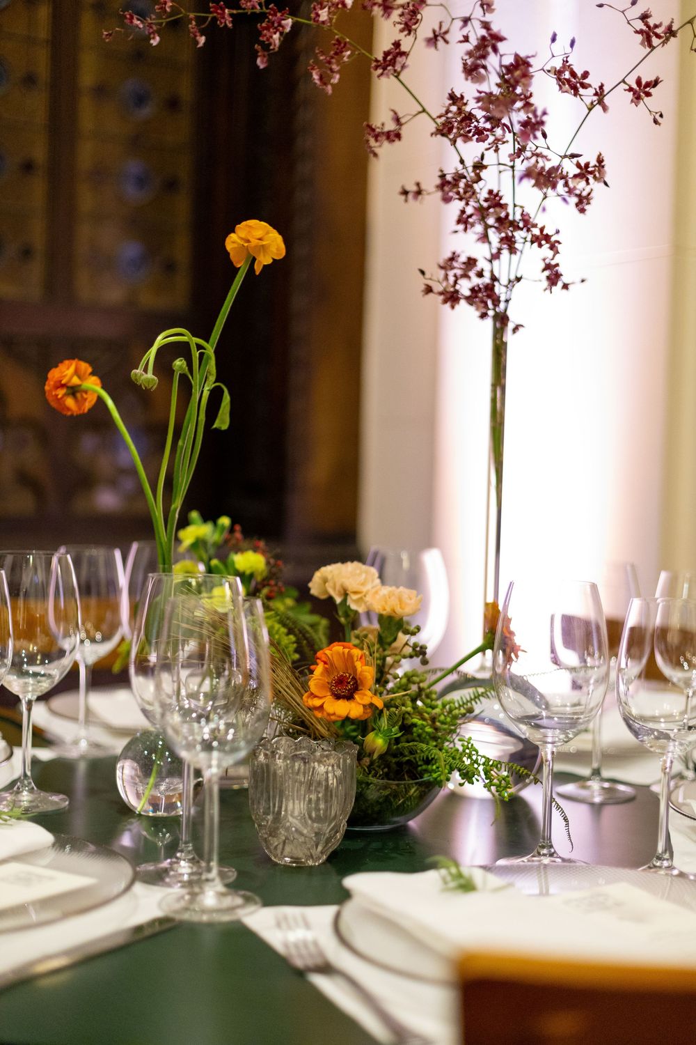 Elegant table setting with crystal wine glasses and orange flowers in delicate vases along a formal dining table.