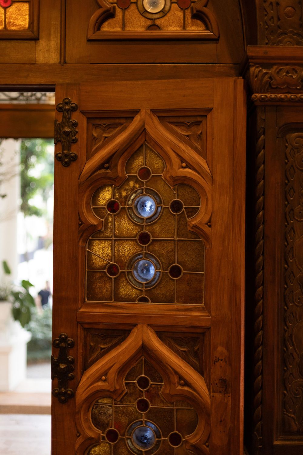 Ornate wooden doors with stained glass panels and decorative gothic-style details in warm lighting.