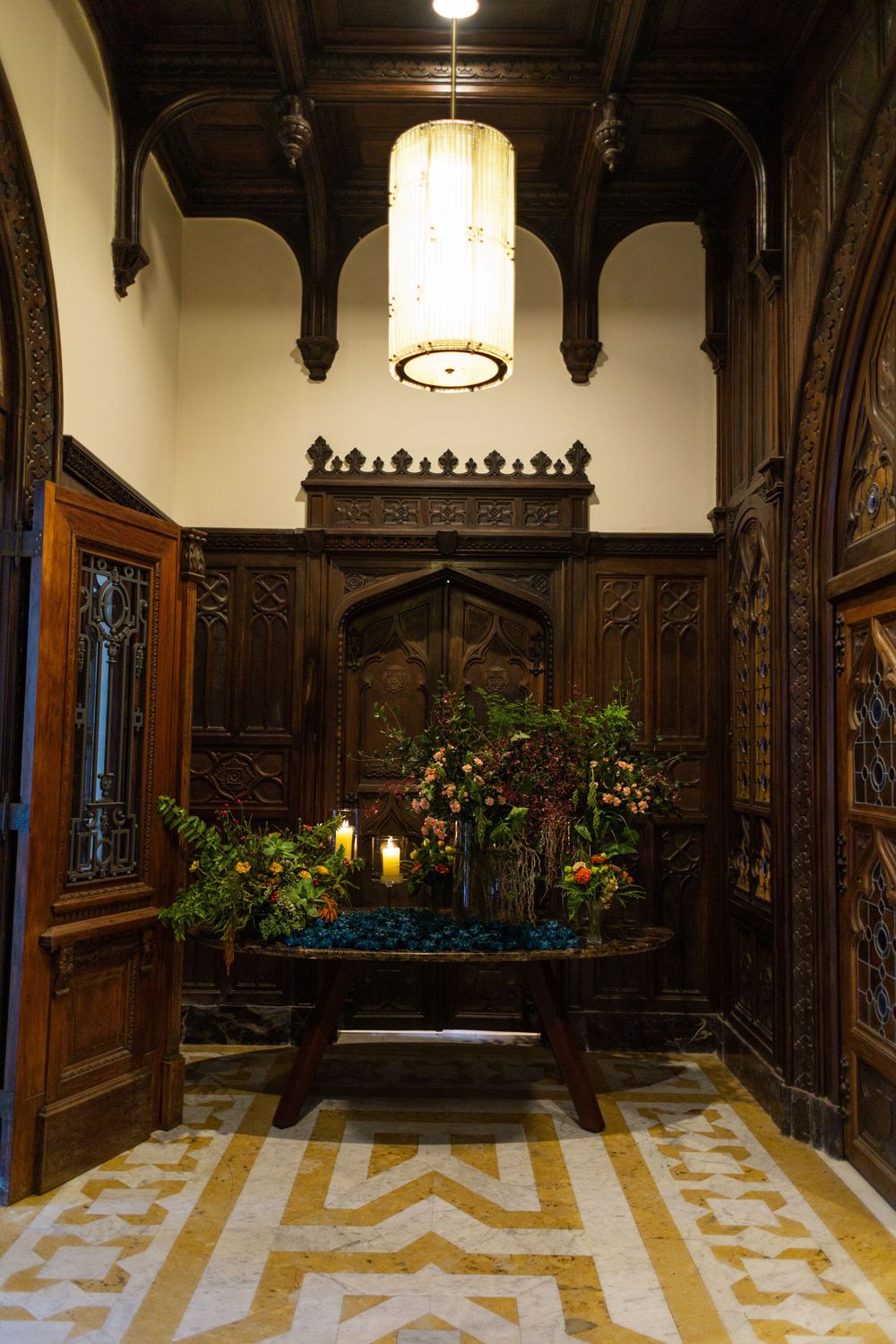 Gothic-style hallway with ornate wood paneling, white marble floors, and decorative floral arrangements.