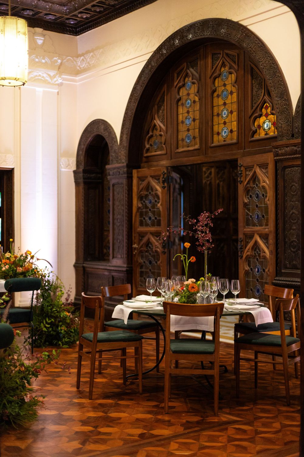 Historic dining space with dark wood arched panels, stained glass windows, and elegant table settings.