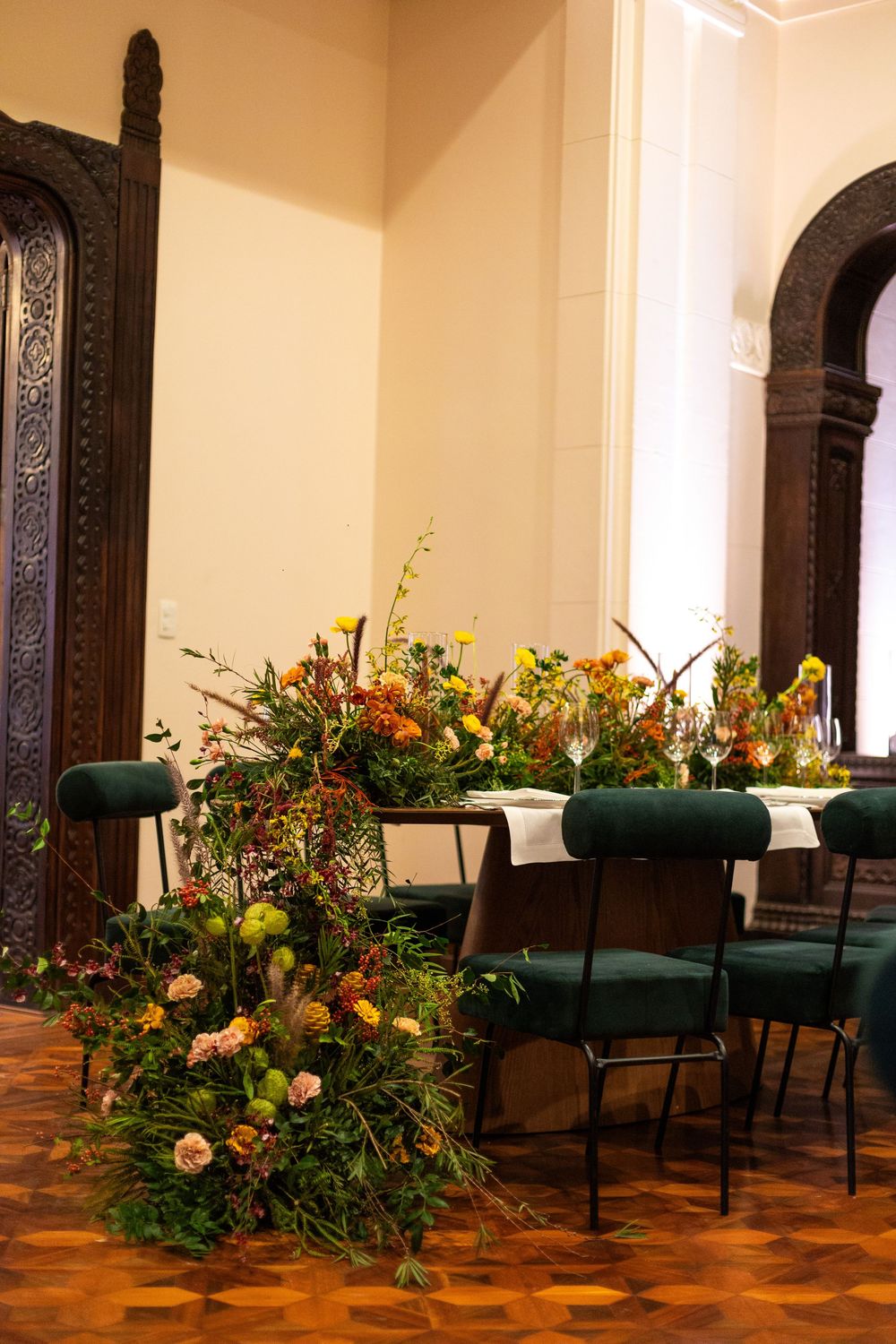 Elegant event space with green chairs and vibrant floral arrangements on wooden floors.