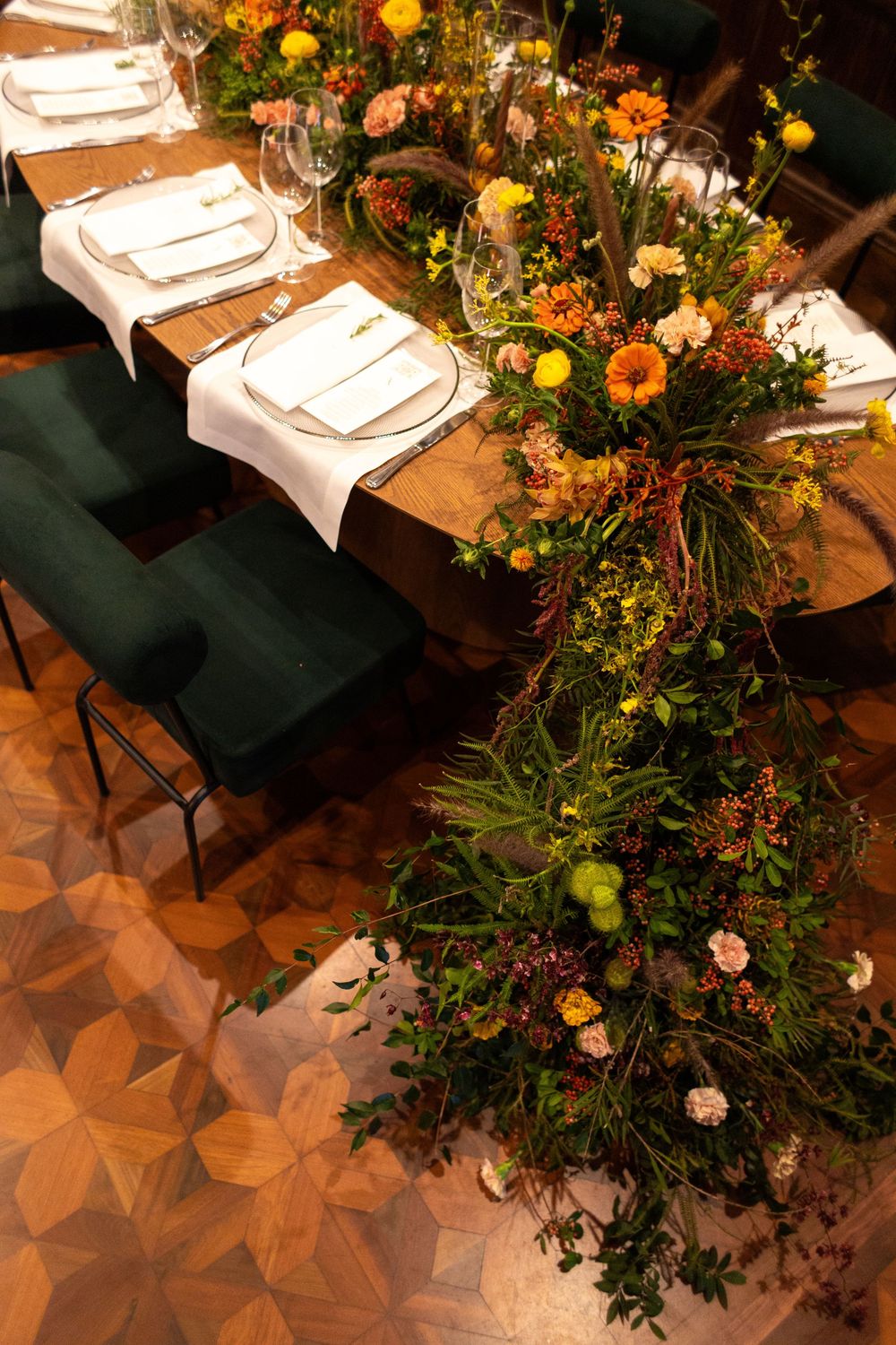 Overhead view of dining table settings with lush floral arrangements and greenery in warm ambient lighting.