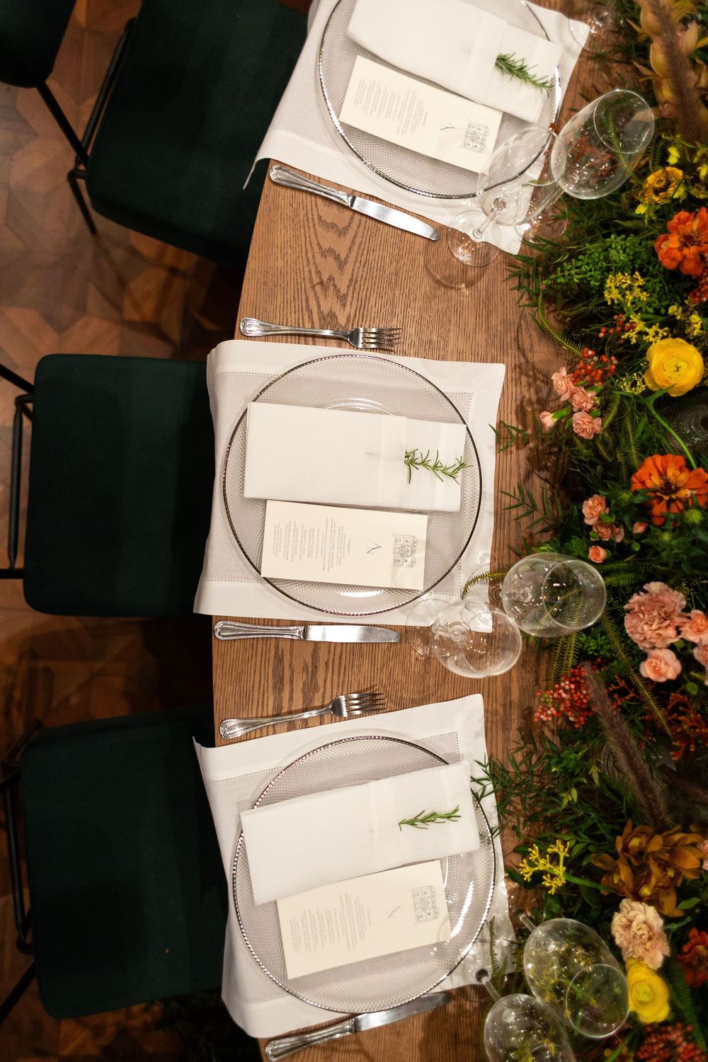 Overhead view of an elegant dinner table setting with white place settings and floral arrangements on a wooden surface.