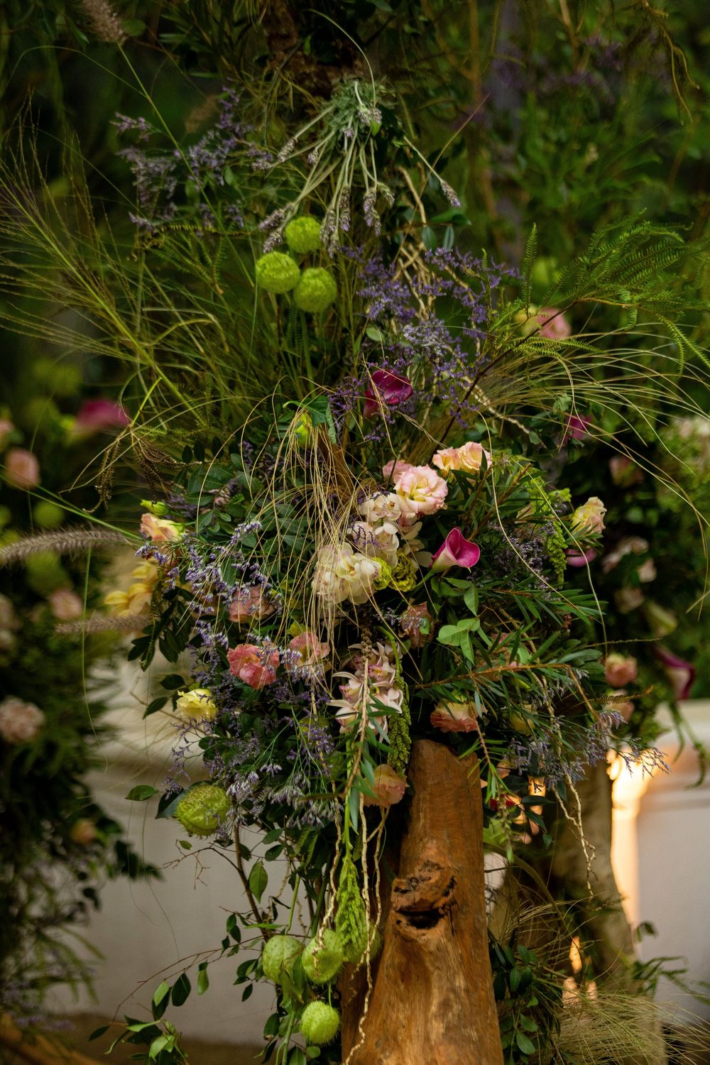 Whimsical floral arrangement with wild grasses and pastel blooms displayed on rustic wooden stands.