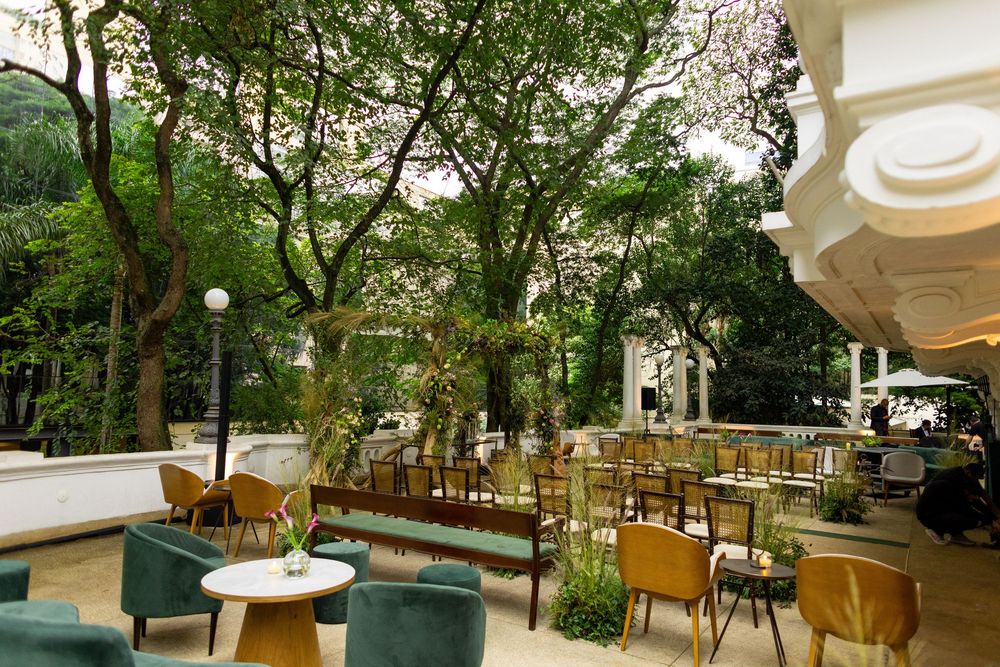 Elegant restaurant interior with white columns and green trees visible through large windows creating a bright atmosphere.