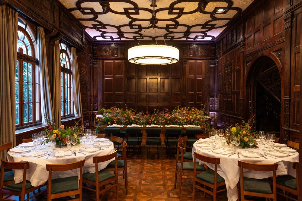 Panoramic view of an ornate dining room with wood-paneled walls, decorative ceiling, and white-clothed tables.