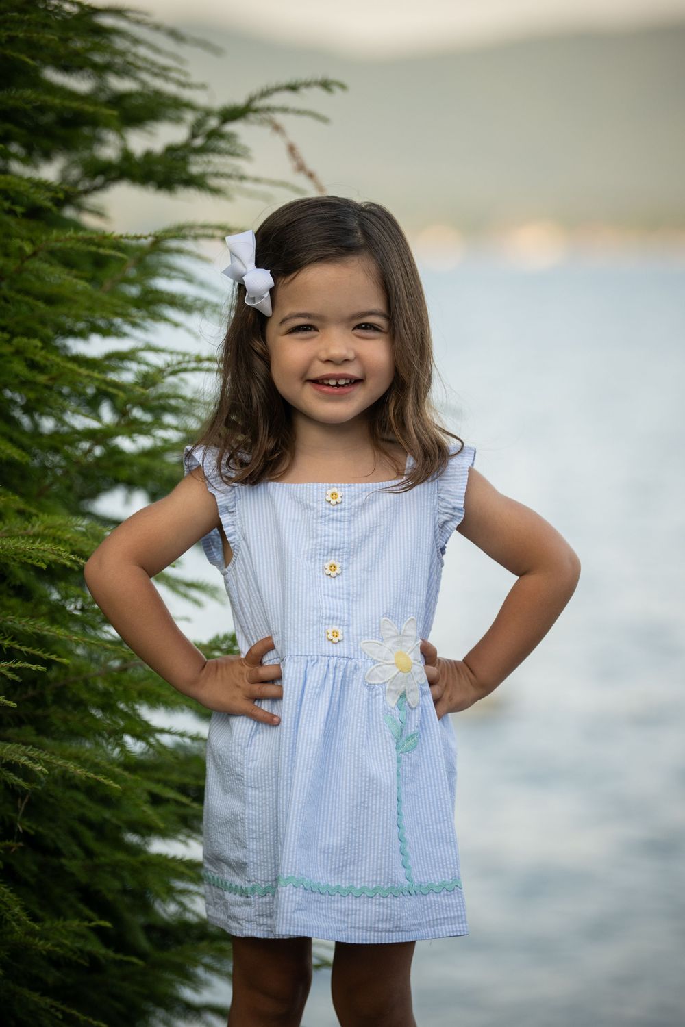 A light blue sleeveless summer dress with decorative buttons against a cloudy sky background.