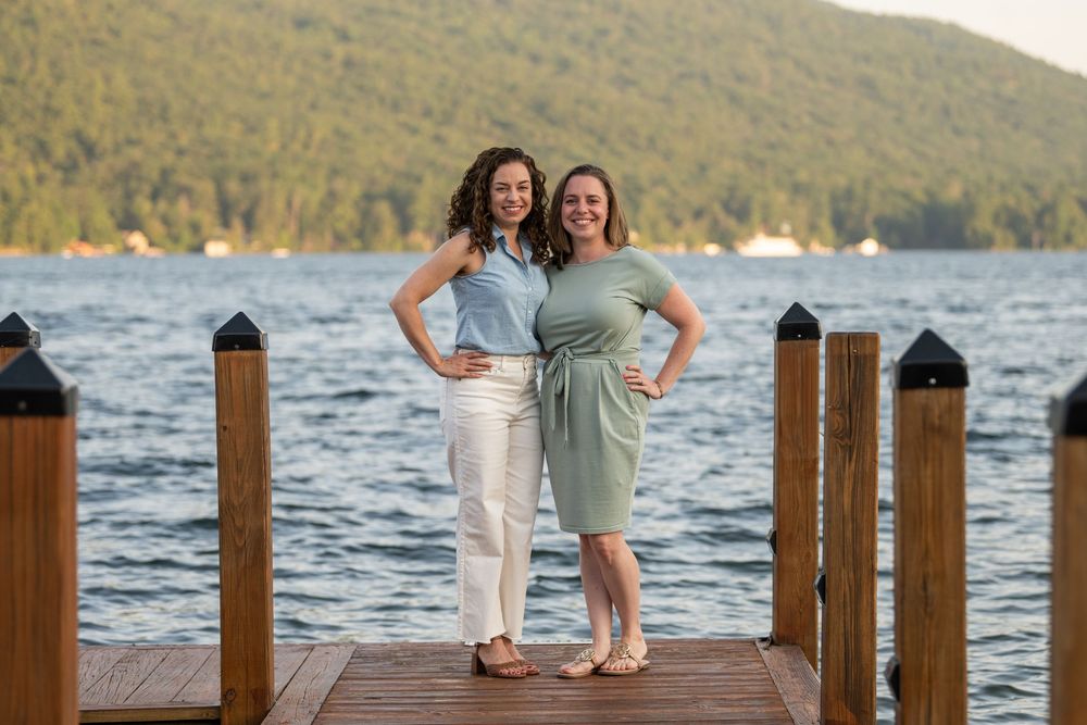 Children play and pose on a wooden dock overlooking a scenic mountain lake at sunset.