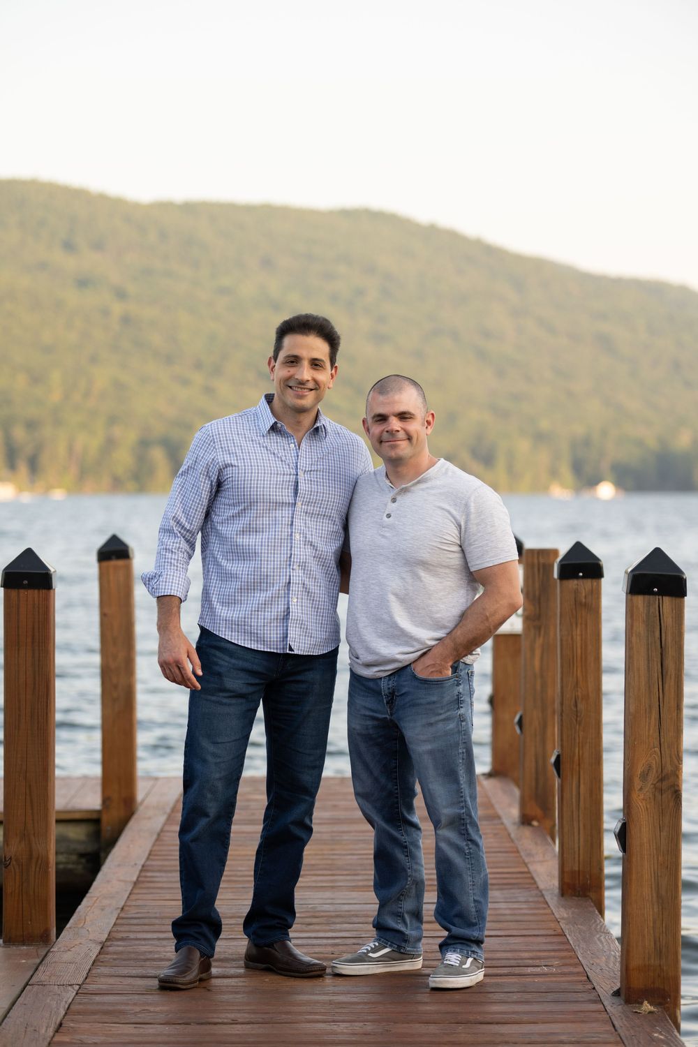 Two people share a moment on a wooden dock overlooking a scenic lake with mountains in the background.