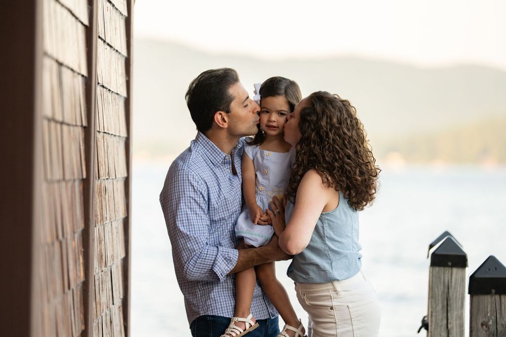A family shares a tender moment together on a dock during sunset by the water.