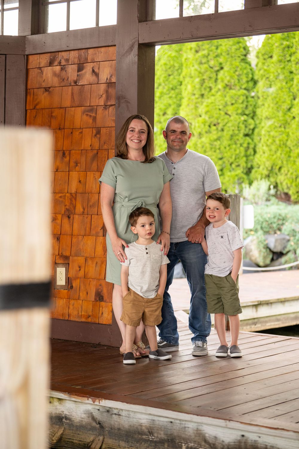 A family photo session on a rustic wooden deck with natural lighting and greenery in the background.