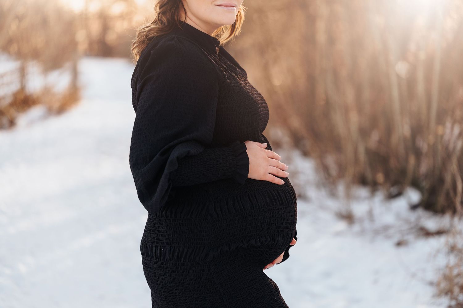 Silhouette of an expectant mother in a black sweater against a snowy winter backdrop.