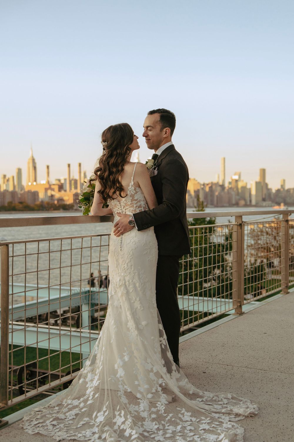 A couple shares a romantic moment at sunset with the New York City skyline visible across the water.