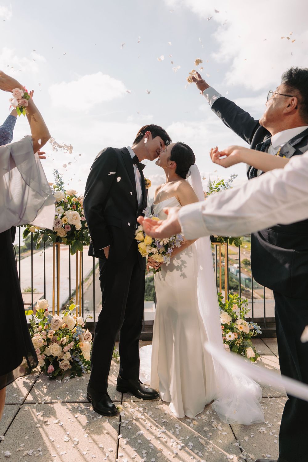Wedding party throws confetti in celebration during outdoor ceremony with floral decorations.