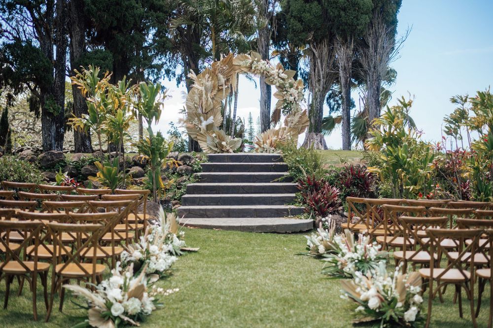 Rustic wooden chairs line up on a green lawn for an outdoor wedding ceremony with white floral arrangements.