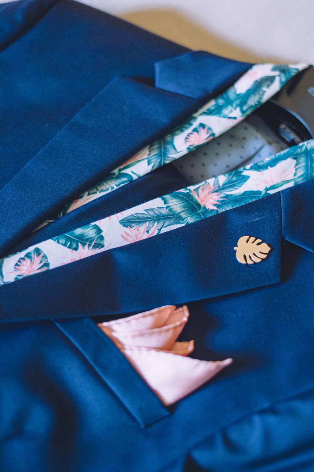 A series of images showing tropical floral pattern fabric being folded into a pocket square on a navy blue suit.