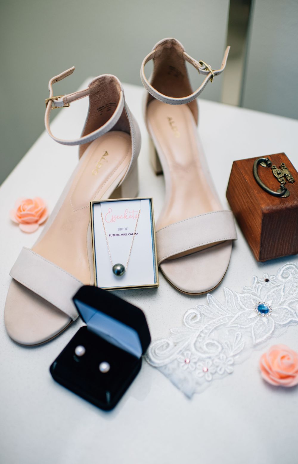 Elegant bridal accessories including white heels, pearl jewelry, and lace details on a white surface.