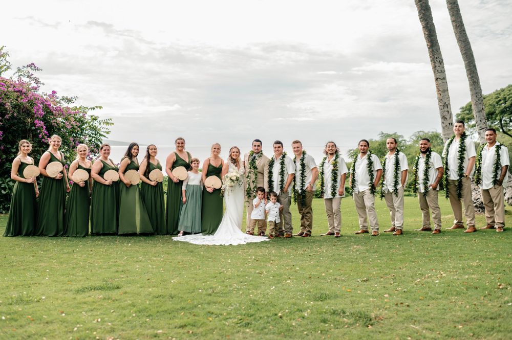 Full wedding party portrait with bridesmaids and groomsmen under palm trees.