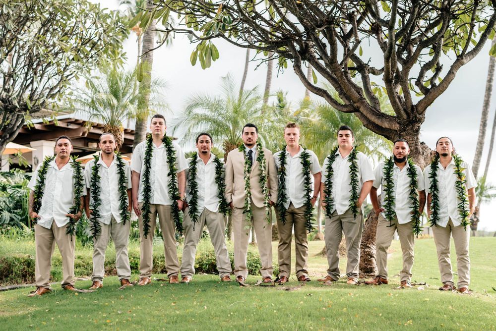 Groomsmen in khaki suits lined up for formal wedding photo on tropical grounds.