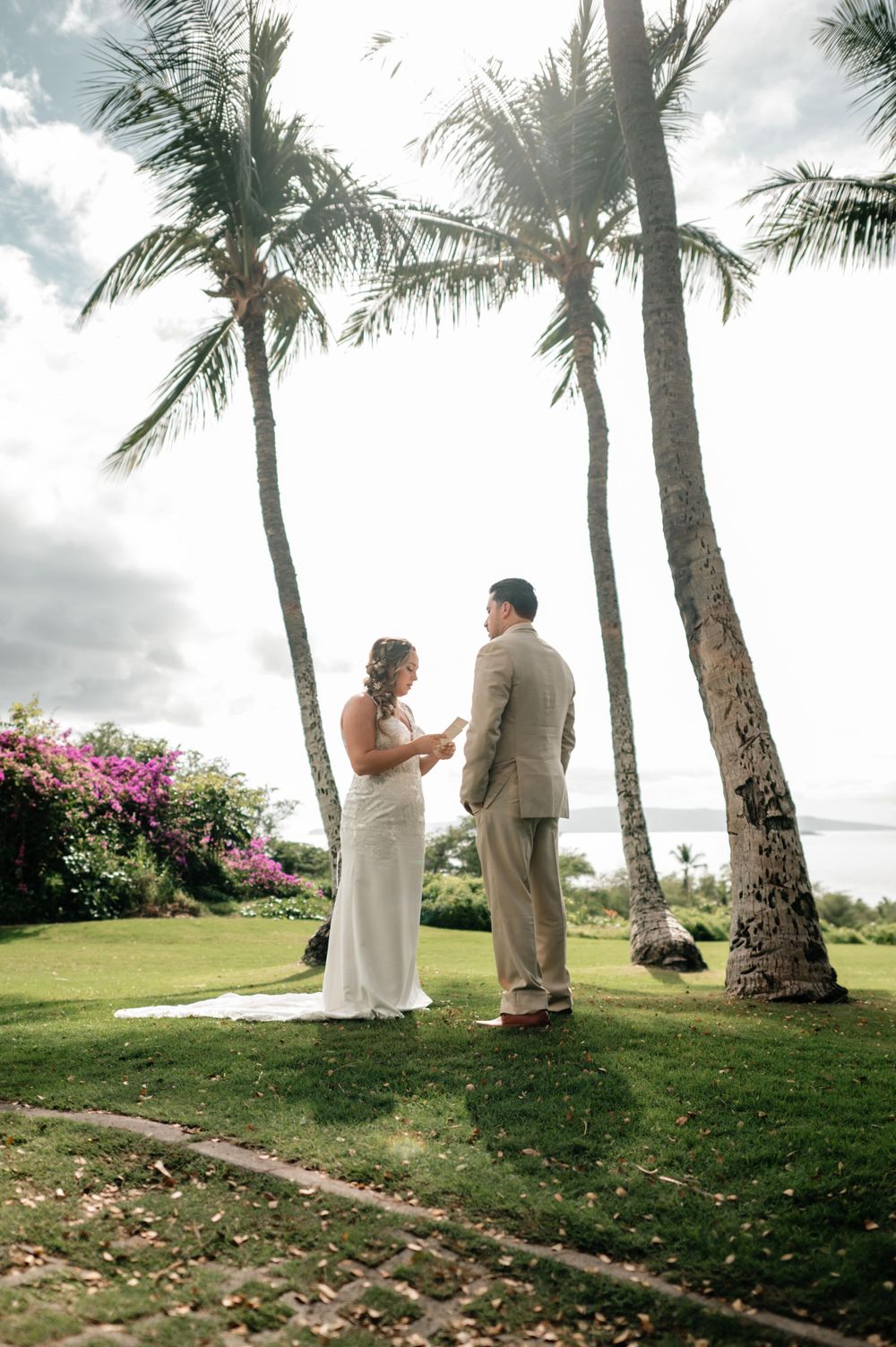 First look wedding moment captured between palm trees on a scenic tropical lawn.