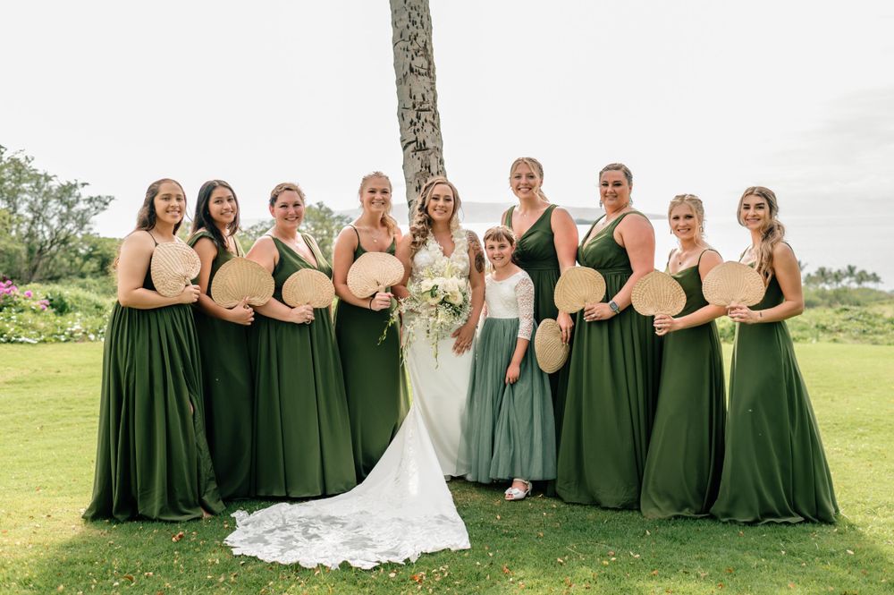 Bridesmaids in elegant dark green dresses pose together on a grassy lawn.