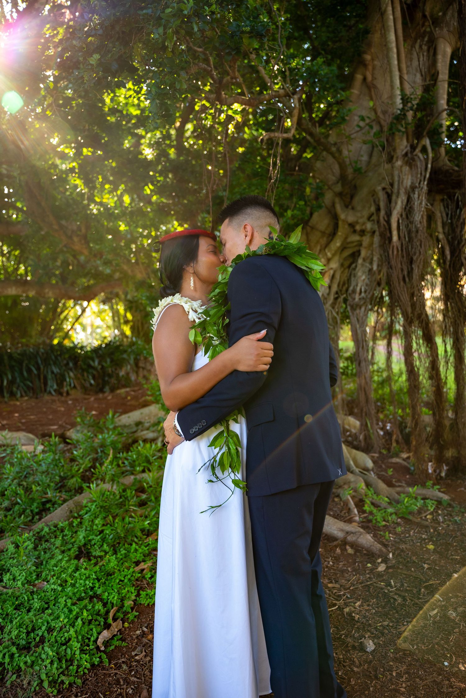 A couple in a white dress and dark suit share a romantic moment in a lush garden setting.