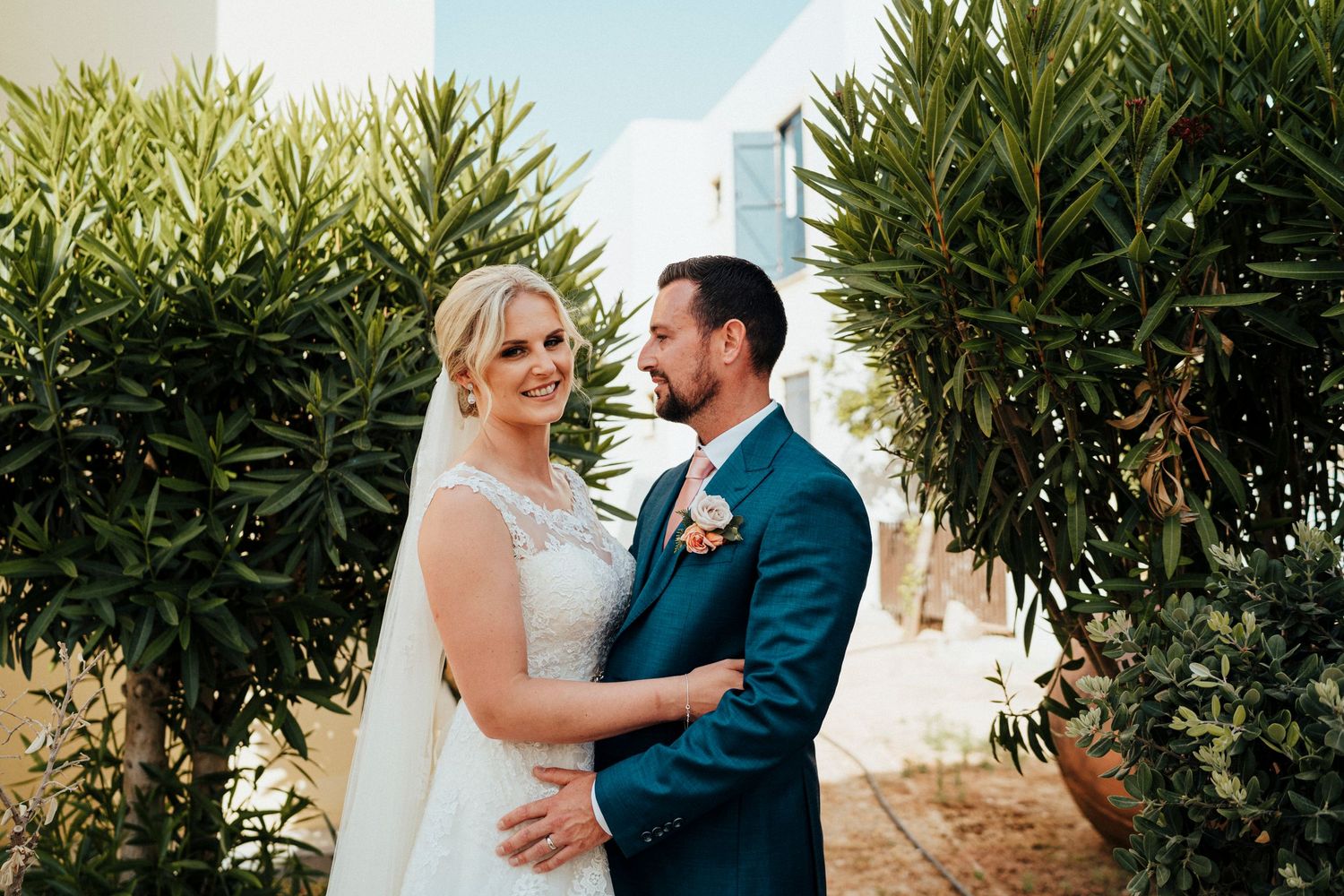 A romantic wedding moment captured among lush greenery with two people embracing in formal attire.