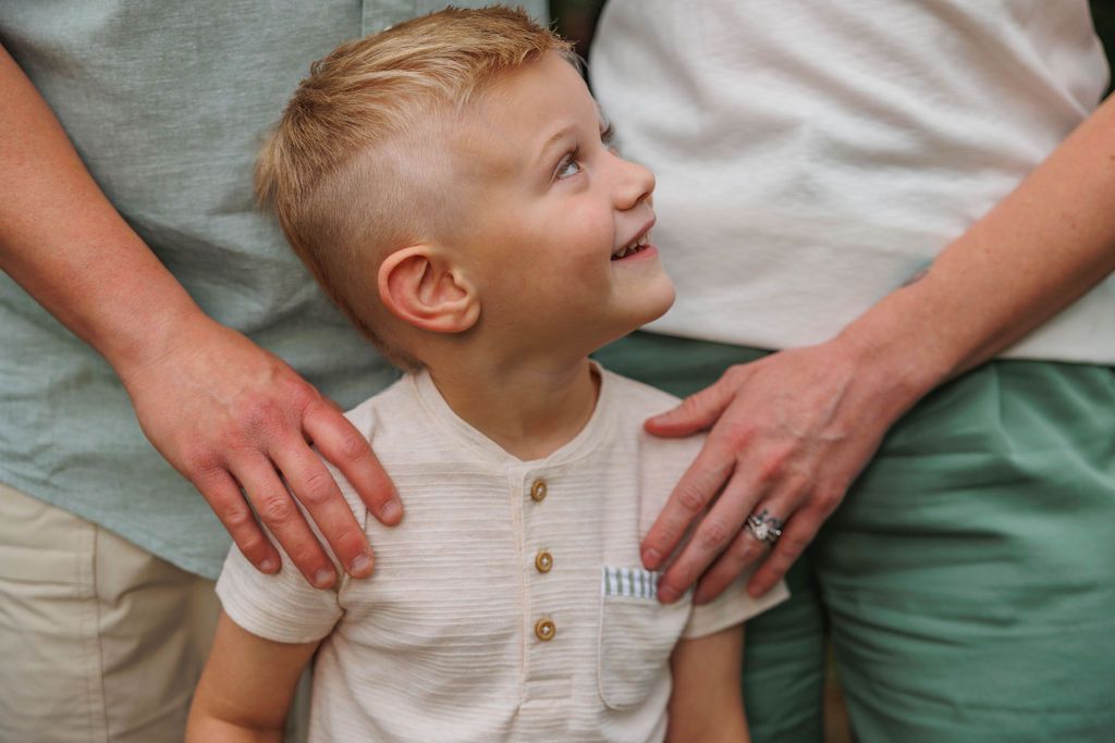 A young child in a white shirt sits and laughs while being comforted by adult hands.