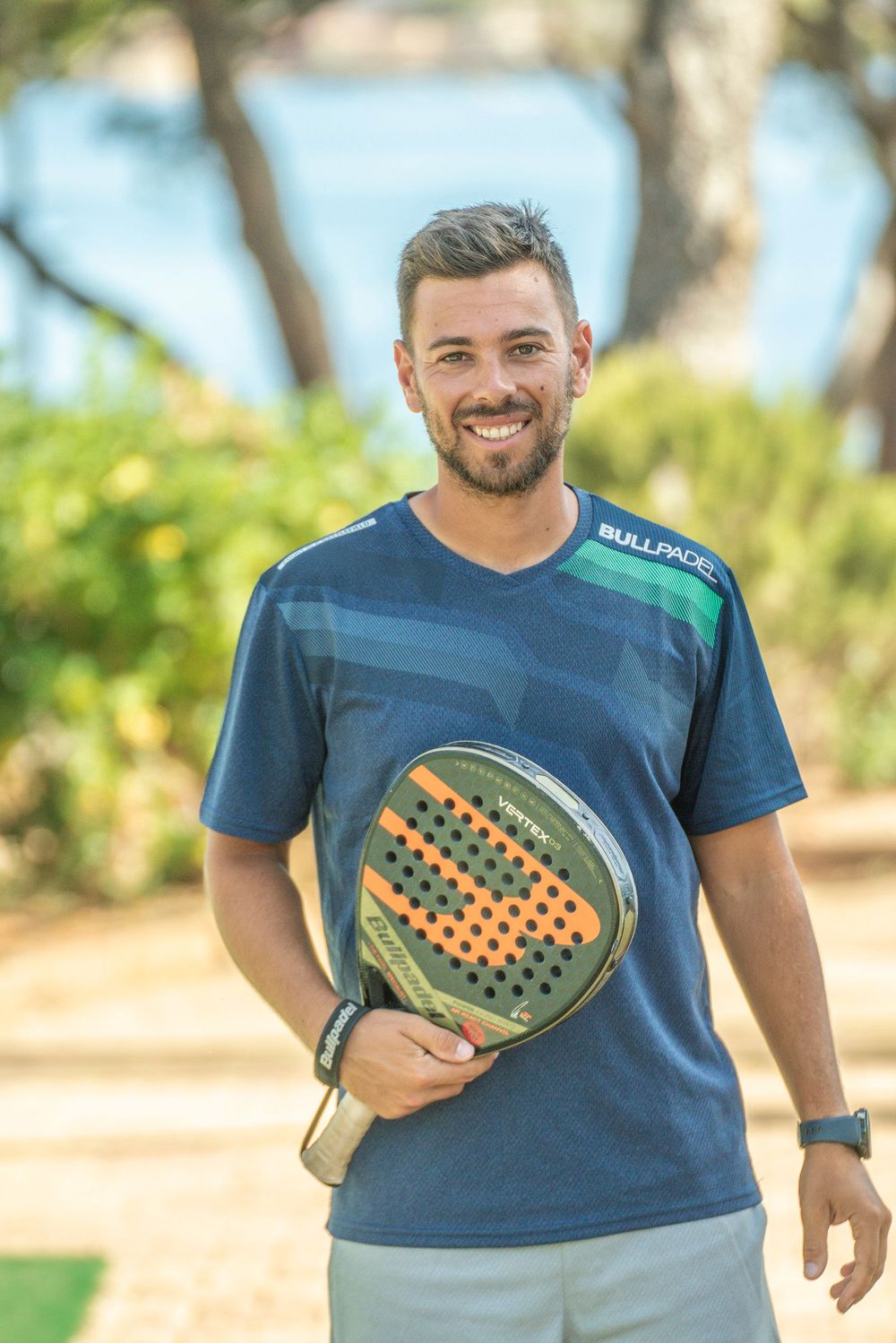 Person wearing a navy blue t-shirt with a pickleball paddle design smiles outdoors in natural lighting.