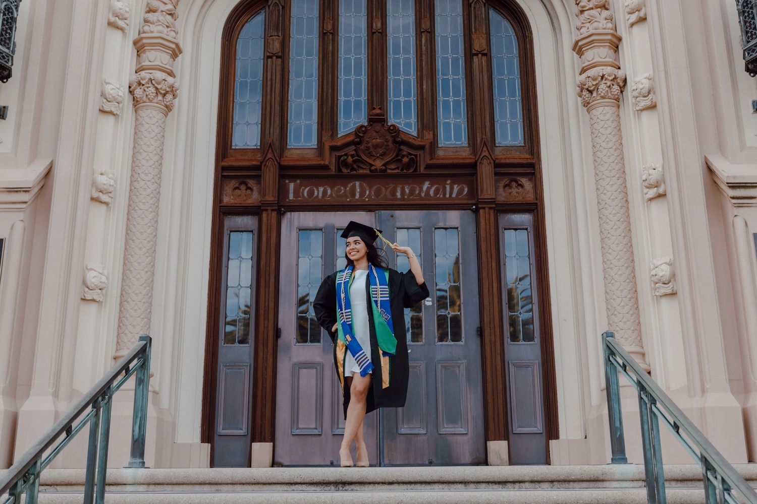 College graduate holds tassel on the steps of Lone Mountain at the University of San Francisco. Taken by Bay Area Graduation Photographer.