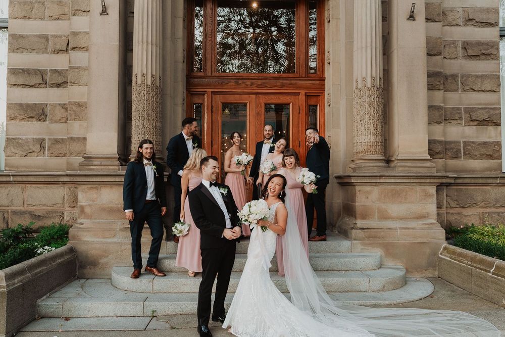 Wedding party poses on steps of historic stone building with bridesmaids in blush pink dresses.