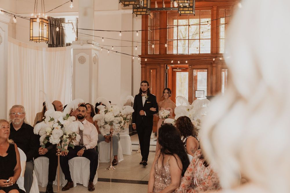 Groom walking down the aisle at a romantic indoor wedding ceremony with string lights.