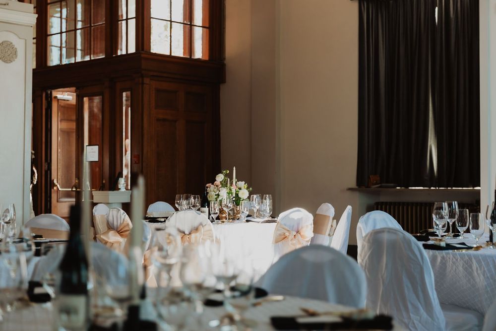 Elegant wedding reception hall with white chair covers and floral centerpieces on tables.